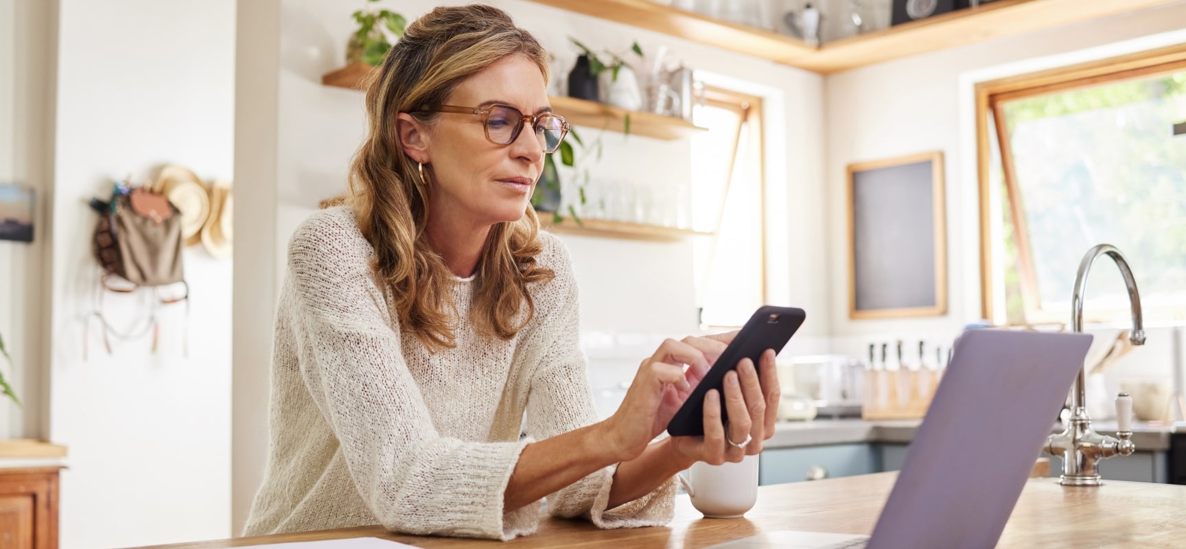 Blonde woman looking at phone in front of laptop