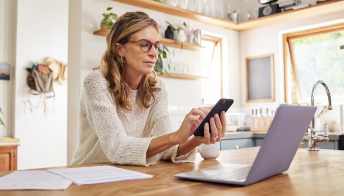 Blonde woman looking at phone in front of laptop