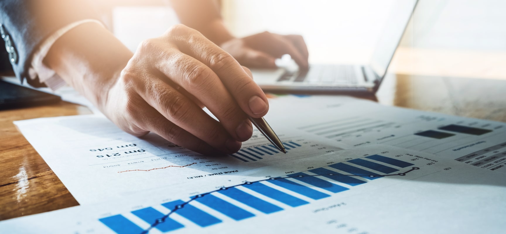 Hand pointing at graphs on desk with a pen