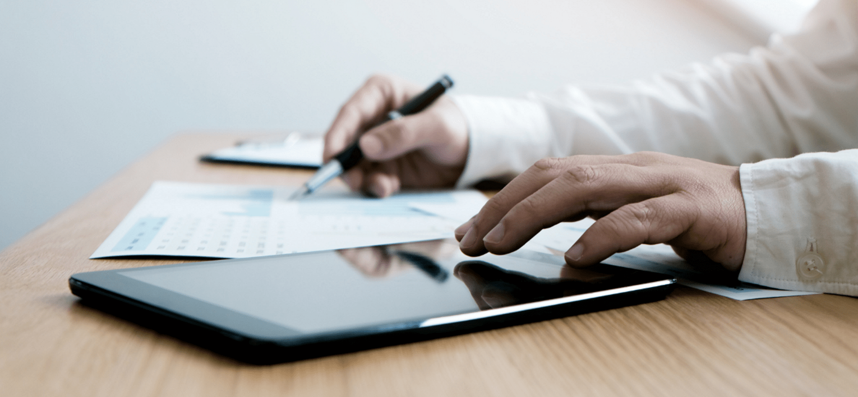 Hands reaching over a tablet on a table and holding a pen
