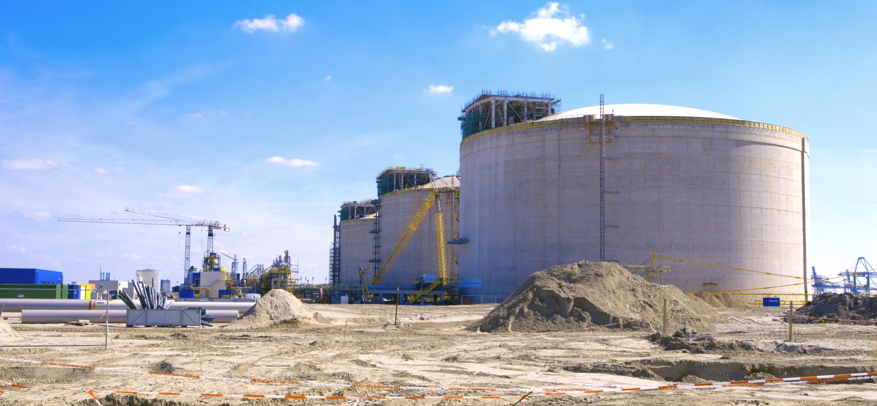 Dry dirt construction yard with crane and cylindrical buildings in background