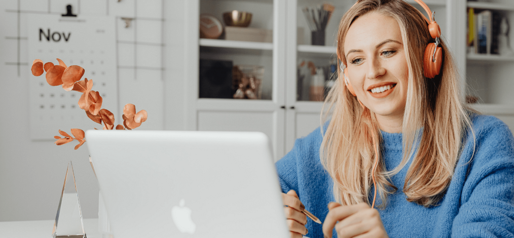 Blonde woman wearing headphones and smiling at a macbook