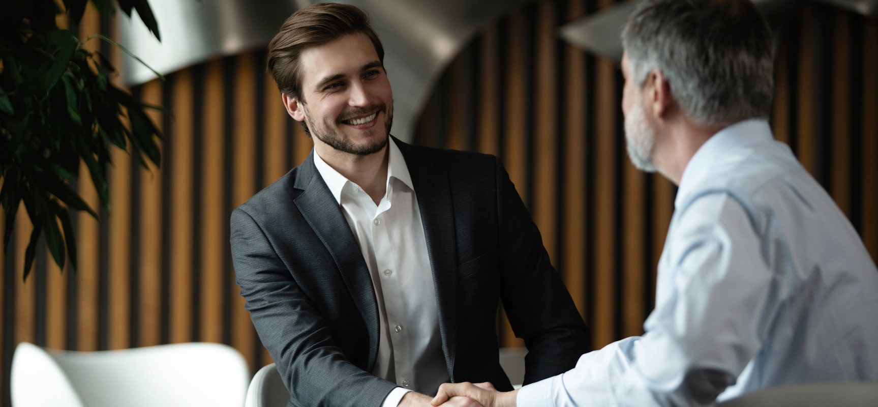 A younger and older businessman smiling and shaking hands