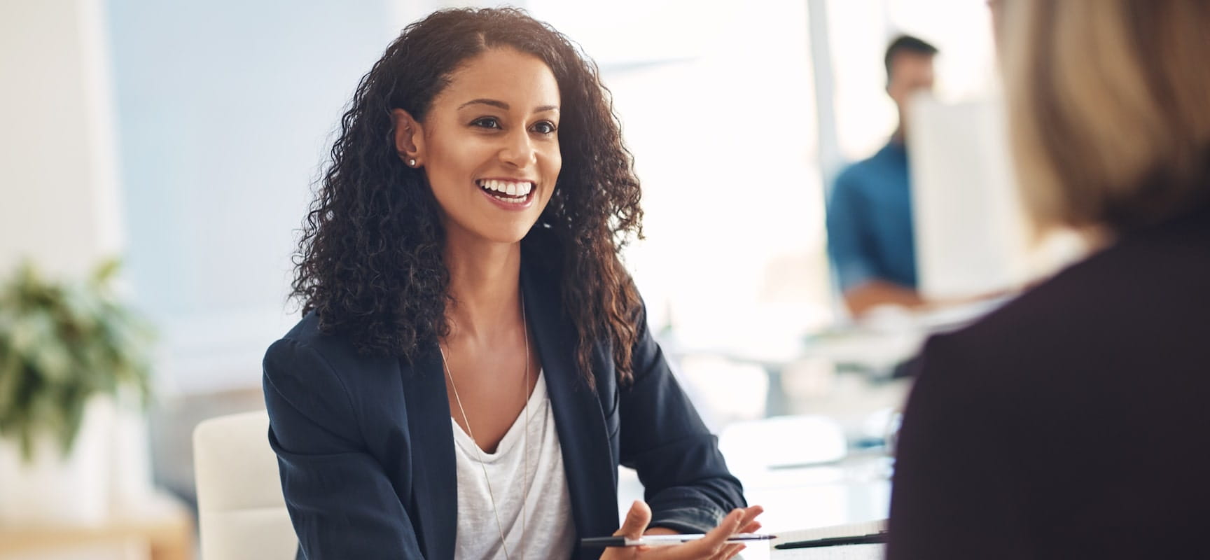 Woman smiling at another woman while holding pen