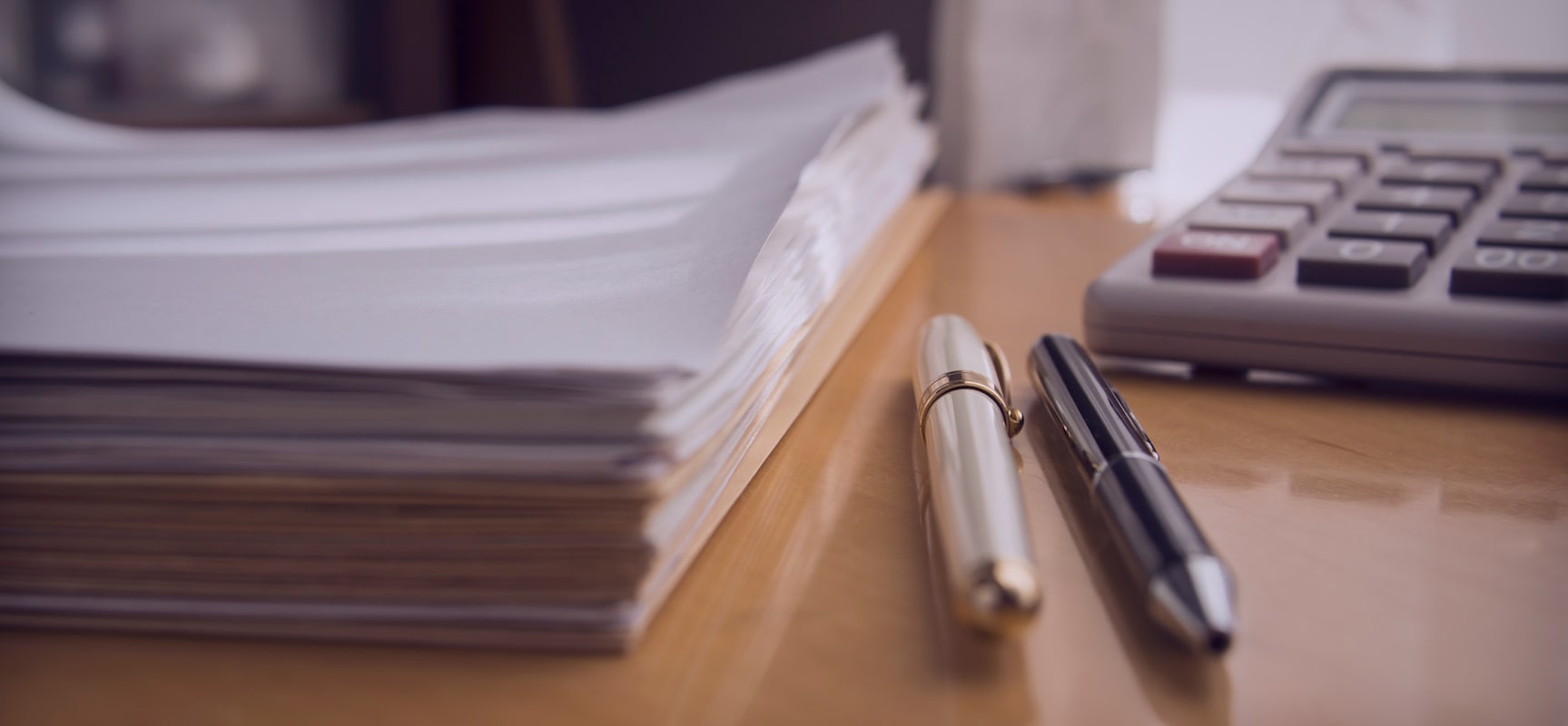 Stack of documents, pens, and a calculator on a desk